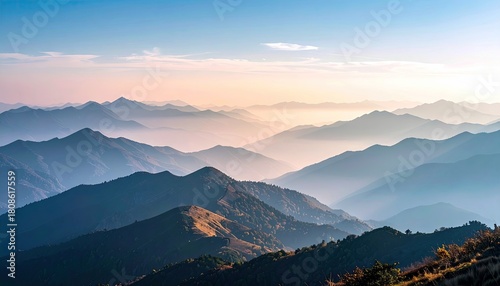 A breathtaking vista of multiple mountain ranges receding into the distance, bathed in the soft light of sunrise and veiled in gentle fog.