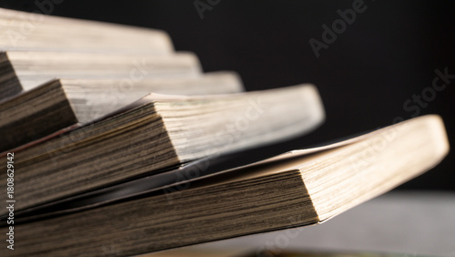 Fotografie Close-up of angled paperback books with layered pages catching warm light, creating a soft abstract pattern suitable for themes of reading, study, or printed media textures