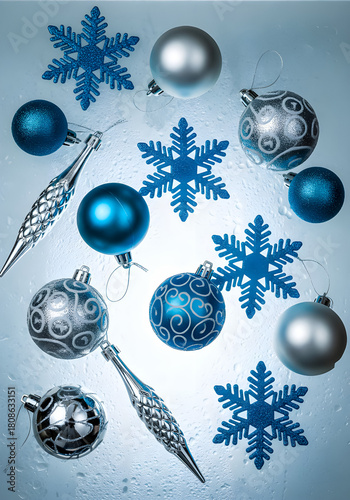 A creative flat lay of Christmas ornaments in various shades of blue and silver, including matte and shiny spheres, textured ornaments, and glittery snowflake cutouts.