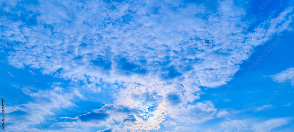 Obraz premium A dramatic view of bright sunlight breaking through thick,fluffy white cumulus clouds against a vibrant blue sky.