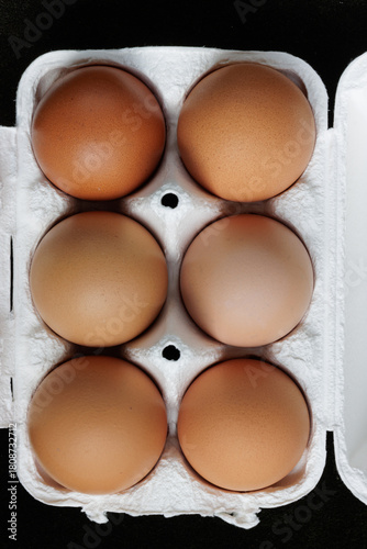 Six different shades of brown chicken eggs in a white cardboard egg box