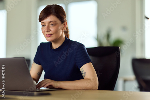 Professional Woman Working On Laptop At Modern Office Desk In Bright Workspace