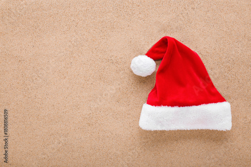 Bright red hat with white fur on dry sea sand background. Closeup. Garment for Christmas celebration. Empty place for text. Top down view.