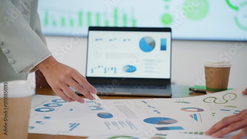 Close-up of two business women analyzing financial data on charts and laptop screen during a team meeting