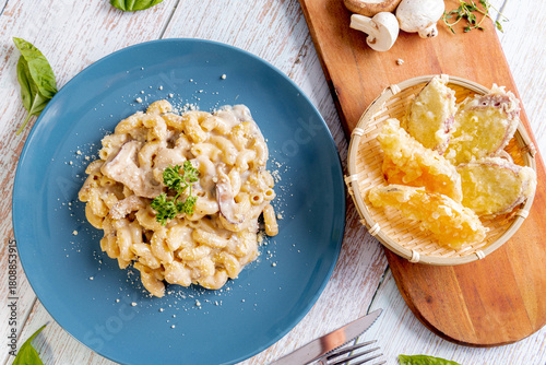 creamy mushroom mac and cheese, served on a blue plate and garnished with fresh parsley. rich cheese and cream sauce with visible slices of mushrooms. Tempura on the side in woven basket