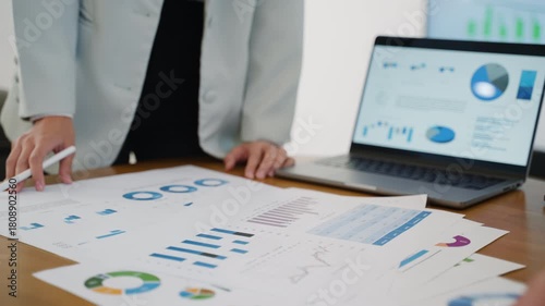 Business team collaborating on financial data and analytics in a modern office. Two colleagues are reviewing charts and graphs while discussing results with a laptop data visuals in the background