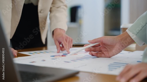 Close-up of two business women analyzing financial data on charts and laptop screen during a team meeting