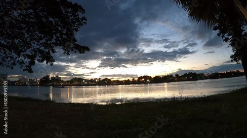 Golden Hour Sunset Cityscape Reflection With Boat Crossing Calm Lake Water.