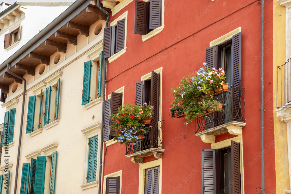 Naklejka premium Cozy balcony in Verona, an Italian town with warm architecture and charming details. Peaceful Mediterranean atmosphere, flowers, sunlight, and traditional building style