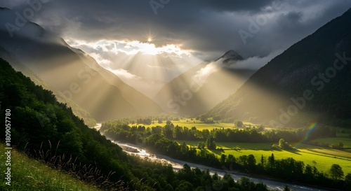 Sun rays through clouds over valley with river and green fields surrounded by mountains and trees