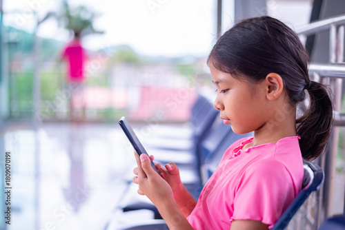 Young Girl Sitting and Using a Smartphone in an Outdoor Waiting Area