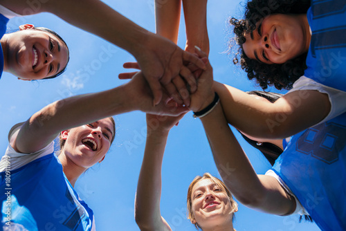 Bild auf Leinwand Female athletes huddling, stacking hands, and celebrating teamwork against a blu