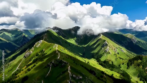 Green alpine mountain ridge panorama with clouds over open valley under blue sky