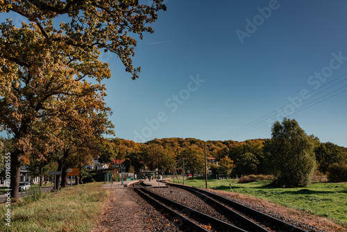 Perspective view of the narrow-gauge railway tracks leading into the distance, lined by trees with early autumn foliage under a dramatic blue sky with wispy clouds.