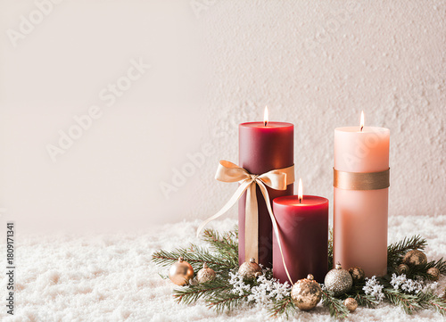 Three burning Christmas candles with gold ribbon and baubles on snow with copy space holiday composition
