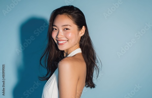 a woman with long dark hair standing against a light blue background. Her white top and even lighting make the details of her face and hair easy to see.