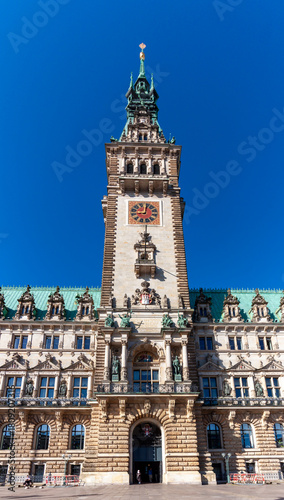 The impressive clock tower and main entrance of Hamburg City Hall (Rathaus) in Germany, captured on a clear, sunny day against a bright blue sky