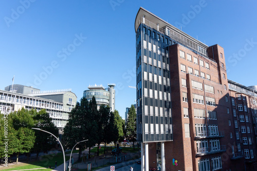A modern office building with a curved glass and brick facade, contrasting with surrounding contemporary architecture in the urban area of Hamburg, Germany