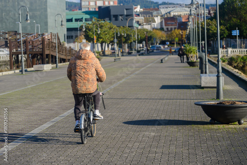 Old man is riding a bicycle down a sidewalk