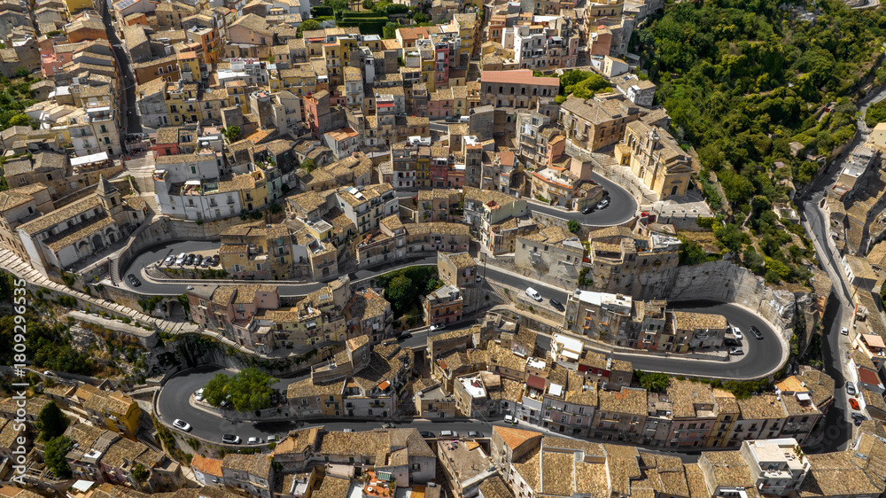 Fototapeta premium Aerial view of a paved road through an Italian hilltop village nestled between the mountains. This is the historic center of Ragusa Ibla, Sicily, Italy.