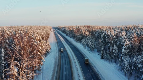 Highway through a snow-covered forest. Aerial view of cars and trucks moving along a highway surrounded by a winter forest.