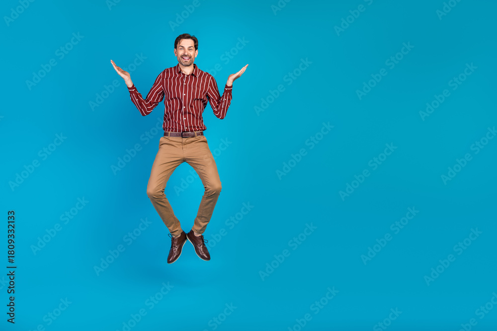 Fototapeta premium Young stylish man jumps in red striped shirt and khaki pants against a blue background perfect for lifestyle fashion advertising