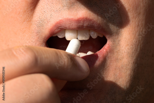 Extreme macro view of a man placing a capsule at his lips; warm sunlight and shallow depth highlight supplement use, vitamin health awareness and a responsible daily lifestyle.