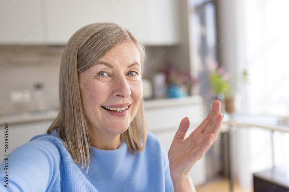 Fototapeta premium Senior woman smiling and talking during a video call, communicating with hand gestures from home, showing connection and accessibility for elderly people
