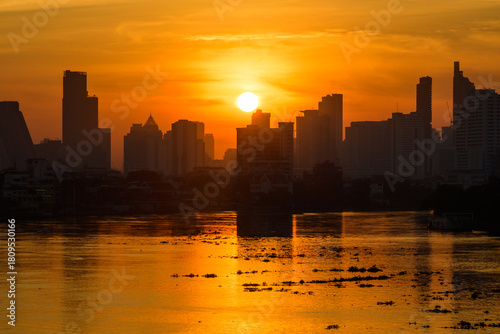Morning sunlight shining over river ferry silhouetted against golden sunrise with urban