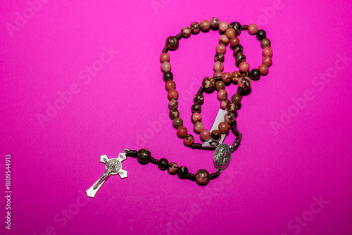 Foto ​A rosary with natural, speckled reddish-brown beads and a metal crucifix and medallion is laid out on a saturated bright pink (fuchsia) background