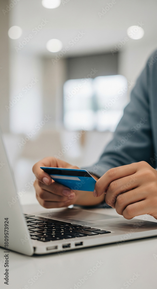 Fototapeta premium Close-up of a blue credit card held by a person near a laptop, representing online purchase, payment or e-commerce transaction