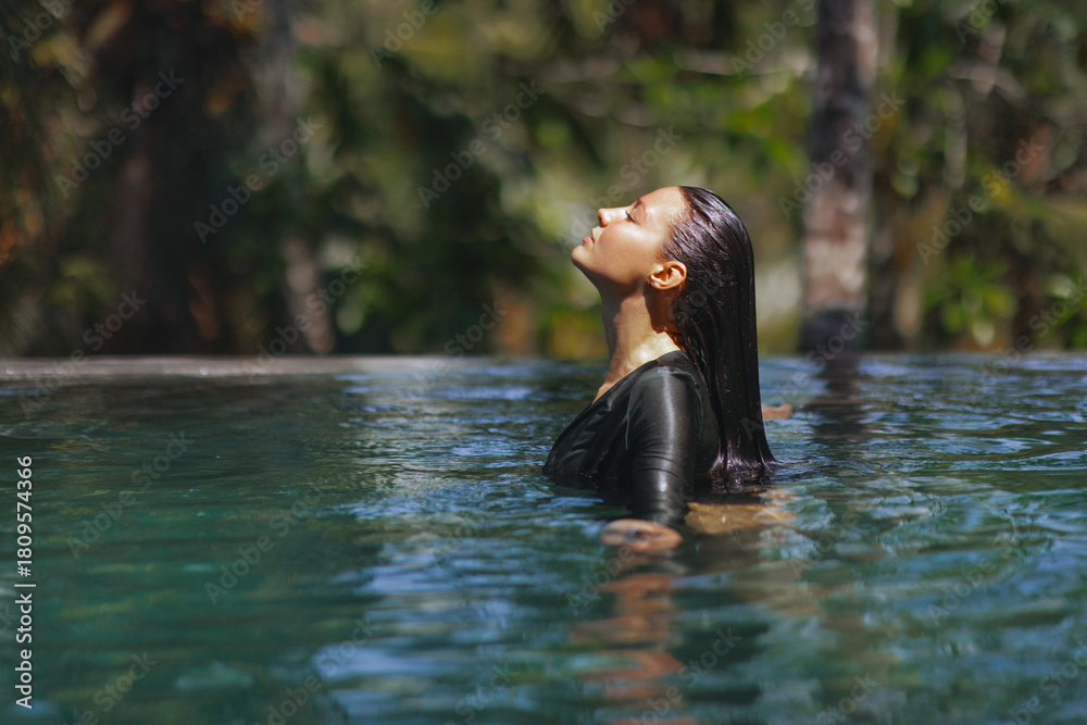 Fototapeta premium Woman Relaxing in Infinity Pool with Eyes Closed Surrounded by Tropical Nature
