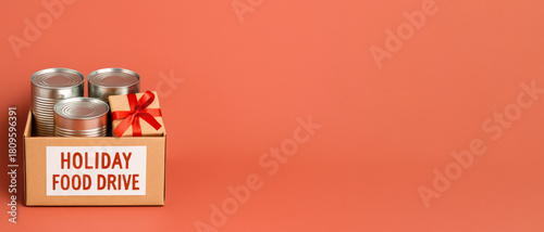 Holiday food drive box with canned goods and gift against orange background