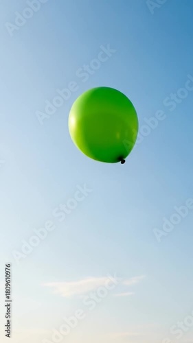 Vibrant green balloon floating skyward in summer breeze, a symbol of joy, hope, and celebration against a clear blue sky backdrop