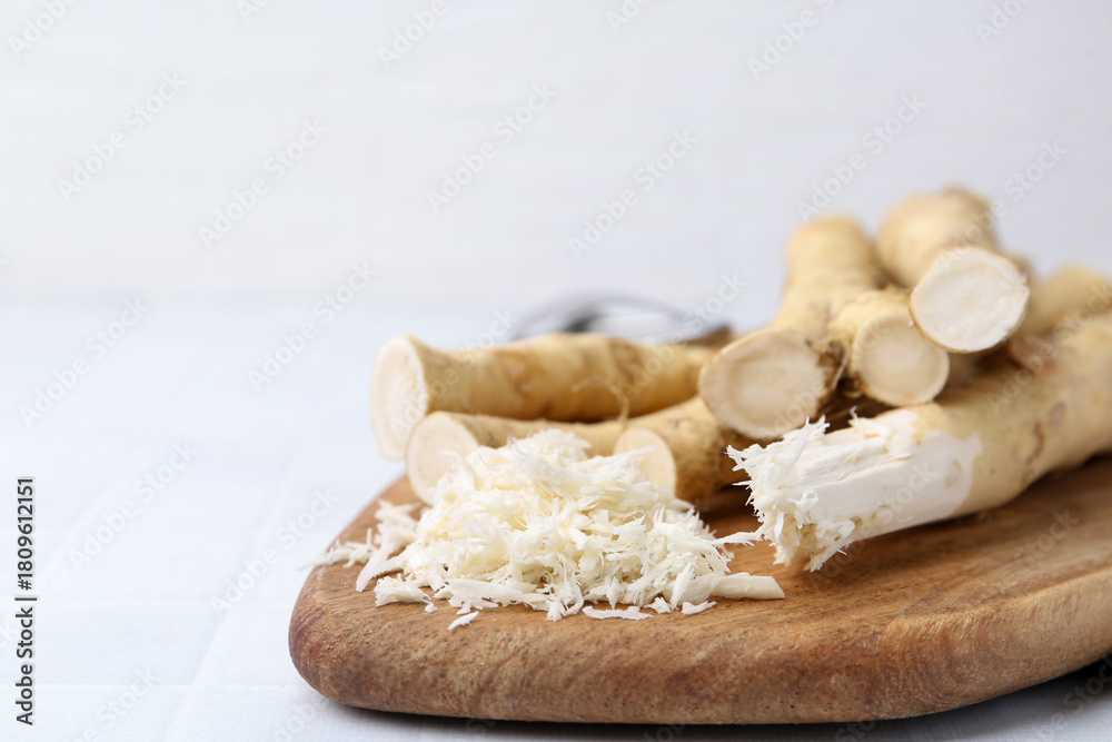 Fototapeta premium Grated horseradish and fresh roots on white tiled table, closeup. Space for text