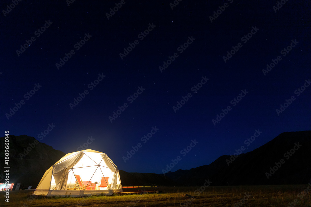 Fototapeta premium Illuminated camping tent under starry night sky in remote mountain landscape