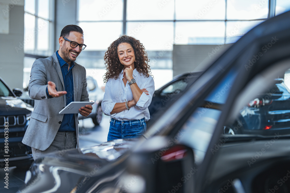 Obraz premium Professional Car Dealership Consultation With Smiling Couple Reviewing Tablet In Showroom During Vehicle Purchase