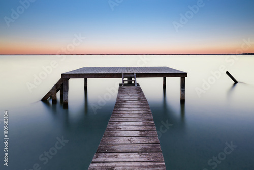 Silent Deck. Longue exposition réalisée au lac de Biscarrosse, où un ponton en bois avance lentement vers une plateforme posée sur l’eau calme. 