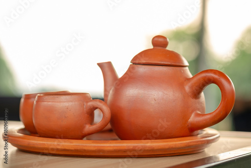 Traditional clay teapot and cups (Teh Poci) from Central Java on a tray. A rustic earthenware tea set, typical of Tegal culture, serving hot tea against a blurred background.
