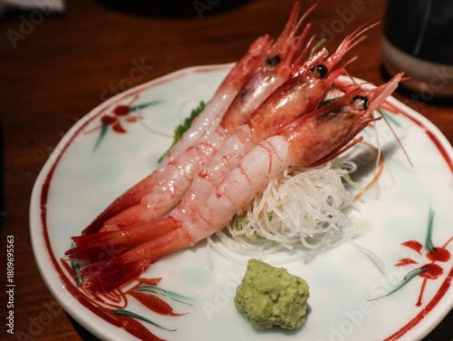 close up of Japanese raw uncooked three prawn sashimi with shell removed, on a floral plate and wasabi on the side