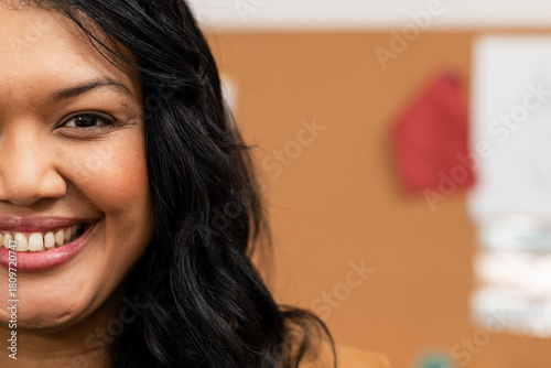 Woman smiling wearing mustard blazer reviewing pinned papers on corkboard in office, copy space