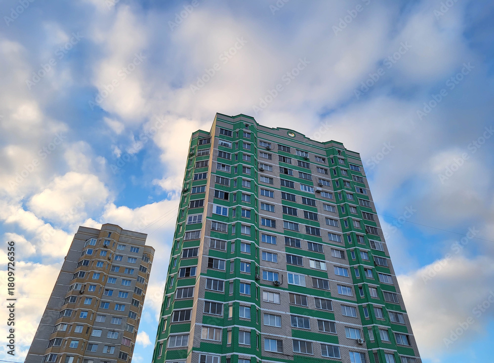 Fototapeta premium Against the background of a blue sky with clouds, there is a modern building with many windows and balconies. I am looking at the facade of a new building.