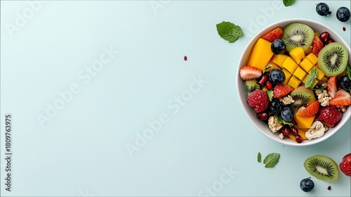A colorful and refreshing fruit salad is presented in a white bowl, featuring a variety of fresh fruits and mint leaves against a soft blue backdrop.