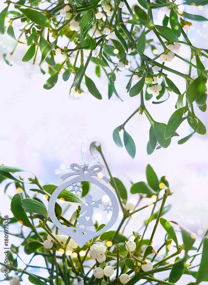 Naklejka premium Mistletoe branches with christmas decor on light abstract background close up. Tradition decor for Christmas holidays, festive winter season. Christmas plant mistletoe (Viscum album). soft focus