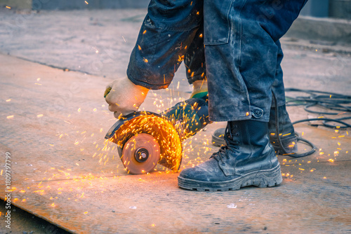 A worker using the electric angle grinder for cutting a metal shift