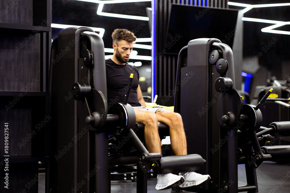 Naklejka premium Man exercising on leg press machine in modern gym with bright lighting