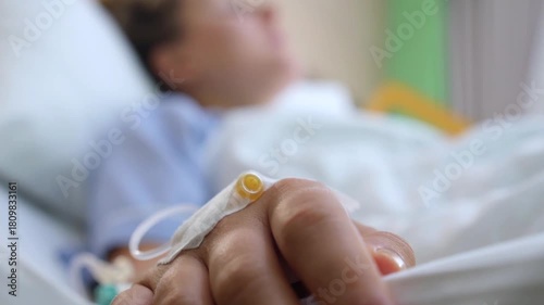 Close up of a patient's hand with an intravenous catheter connected for treatment while resting in a hospital bed, receiving necessary medical care during a period of illness or recovery