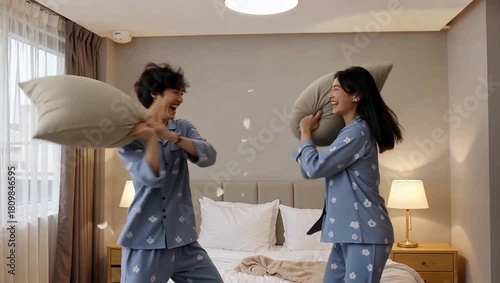 Happy young Asian couple having a fun pillow fight in the bedroom.