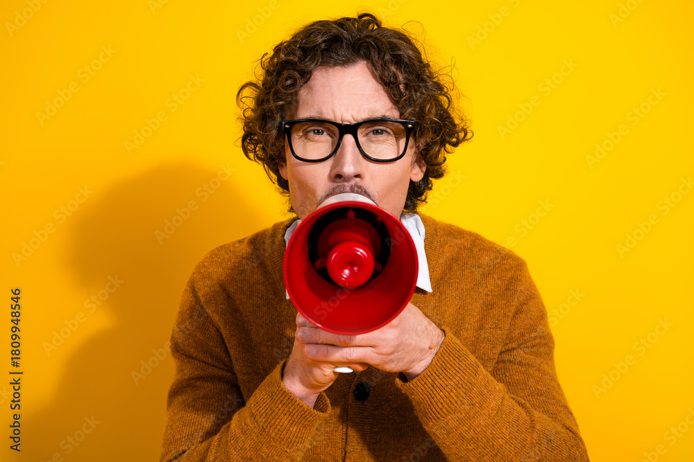 Obraz premium Young stylish man with glasses in a cardigan speaks through a red megaphone against a bright yellow background