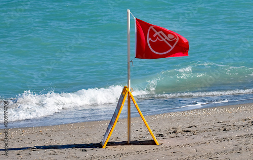 Red no swimming in area flag on a beach with a wave approaching